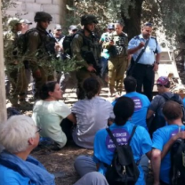 People sitting outside and men in military uniforms surrounding them