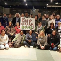 Lots of people in rows posing for the camera holding a sign that says Keep Miriam Home