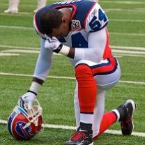Football player wearing red white and blue football uniform kneeling on field