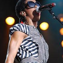 Black woman wearing sunglasses and a striped dress singing into a mic