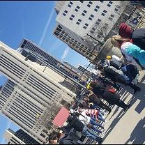 Sideways photo of downtown skyscraper with people standing below protesting