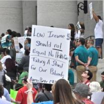 Person holding a sign against the Medicaid cuts at the statehouse with lots of other people