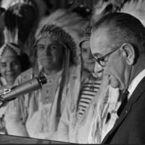 Lyndon Johnson at a mic and Native men in background