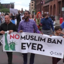People marching outside with sign saying No Muslim Ban Even