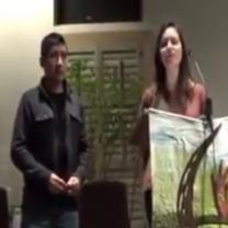 Latino man and white woman standing at front of event speaking