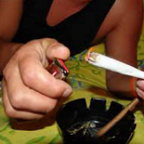 Person's hands closeup one holding a huge joint and the other holding a lighter with an ashtray in the foreground