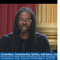 Black man in dreads talking at a mic