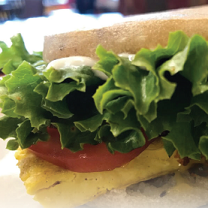 Close up of a sandwich with lettuce and tomato spilling out the side