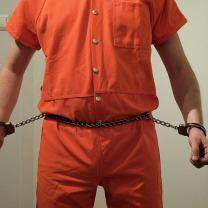 Guy in orange jumpsuit and chain around his belly attached to his wrists