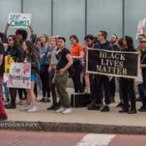 Several young people on a sidewalk at a rally holding a banner saying Black Lives Matter
