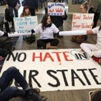 People sitting around a huge banner saying No Hate in our State