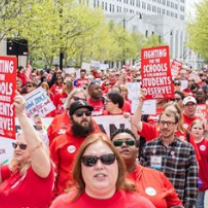 Huge outdoor march with everyone wearing red T-shirts and holding signs that say Fighting for Schools