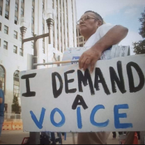 Man holding sign saying I Demand A Voice