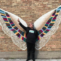 Man standing in front of an art piece of two big wings against a wall