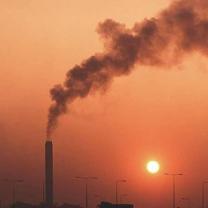 Orange sky with prominent smokestack spewing smoke and sun barely peeking through