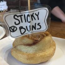 A cinnamon bun with a sign on it saying Sticky Buns