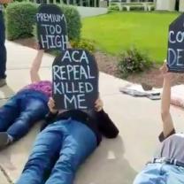 People laying outside on the ground holding tombstone signs that say ACA Repeal killed me