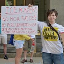 White woman in Black Lives Matter Tshirt holding a sign that says ICE murders