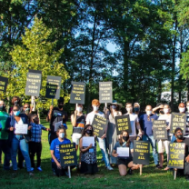 People posing outside by trees with signs