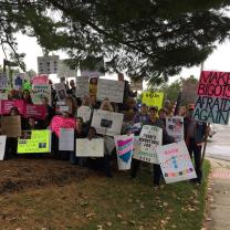 A bunch of people holding signs and facing the camera posing under a tree