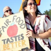 White women with long dark hair and sunglasses holding sun that says Fair Food Taste Better