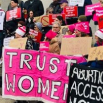 People at a rally holding signs saying Abortion Access and Trust Women