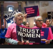 Two older women at a rally holding a sign saying Trust Women