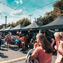 Two young women in the foreground walking through a line of tent booths on a blue-skyed sunny day