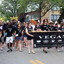 People in black and white Vegan shirts holding Vegan sign marching in parade