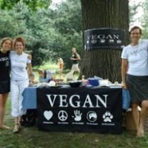 Three happy people by a table outside that says VEGAN on a sign