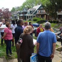 A group with a variety of black and white, old and young people standing outside in a neighborhood with trees and houses