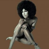 Sixties-looking photo of naked black woman covering up her private parts with arms and legs, she has a huge Afro against a brown background