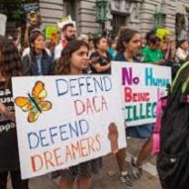 Young people holding signs outside a building that say Defend DACA Defend Dreamers