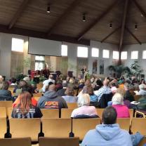 People sitting in chairs in a big hall with their backs to camera