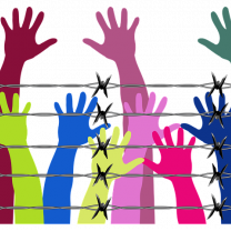 Different color arms and hands reaching up behind a barbed wire fence