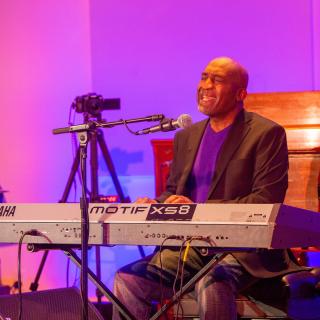 Bald black man singing at a keyboard