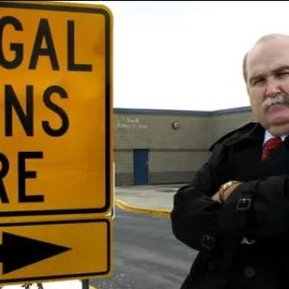 SIgn saying illegal aliens here and a stern bald older man with arms crossed and 