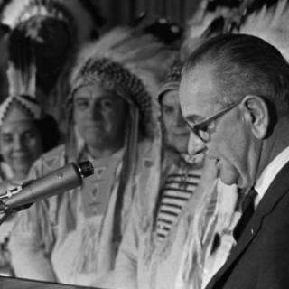 Lyndon Johnson at a mic and Native men in background