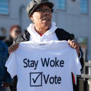 Woman holding T-shirt saying Stay Woke Vote