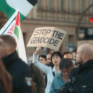 Woman holding sign at rally saying Stop the Genocide
